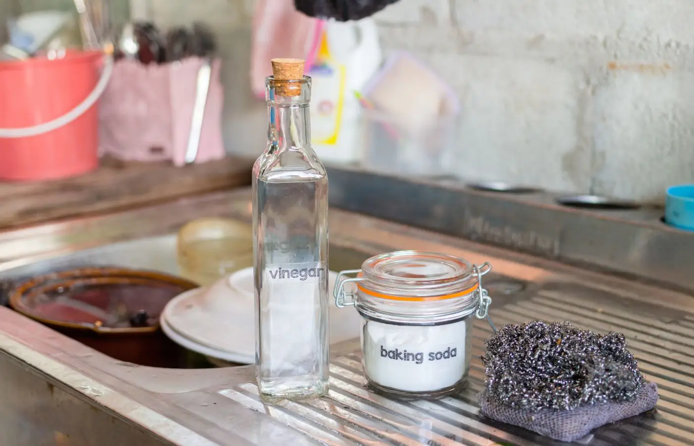 Bouteille de vinaigre et pot de bicarbonate de soude posés près d’un évier, illustrant des solutions naturelles pour entretenir les canalisations.